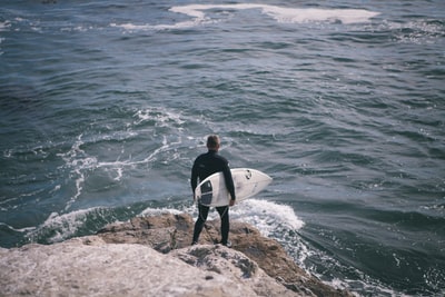 Man standing in front of the sea with a surfboard
